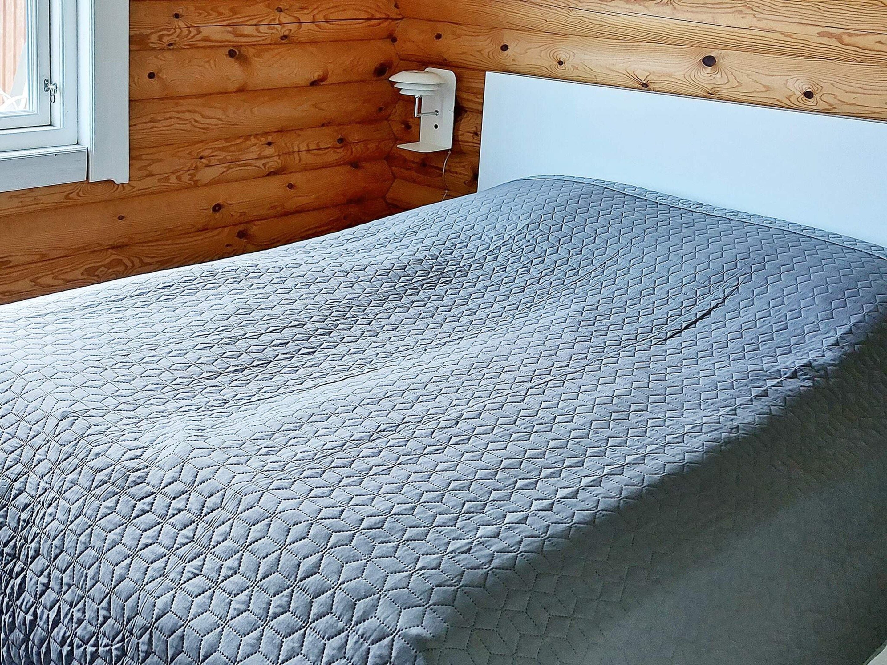 Una cama con cubrecama acolchado en una habitación con paredes de madera y cabecera blanca.