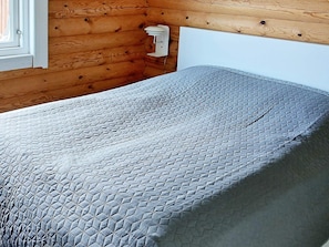A bed with a quilted cover in a room with wooden walls and a white headboard.
