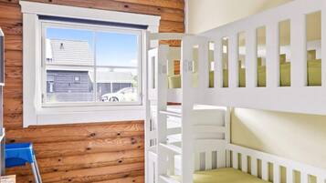 A room with a bunk bed, wooden wall paneling, a window with a view of a house, and a blue chair.