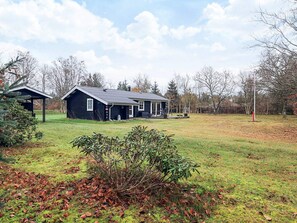 Une maison à deux étages avec un porche, entourée d’une cour verdoyante et d’arbres.