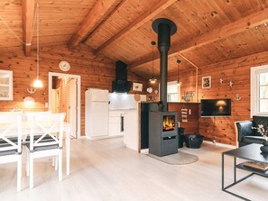 A wooden interior with a central wood stove, white furniture, and a television mounted on the wall.