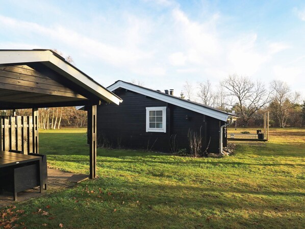 A black wooden house with a white window, a covered porch, and a grassy yard.