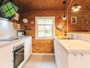 A kitchen with wooden walls, a window, a sink, and a stove.