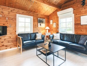 A cozy cabin interior with a wooden interior, a black leather sofa, a coffee table, and a television mounted on the wall.