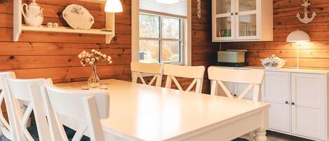 A wooden interior with a white table and chairs, a window with blinds, and a cabinet with glass doors.