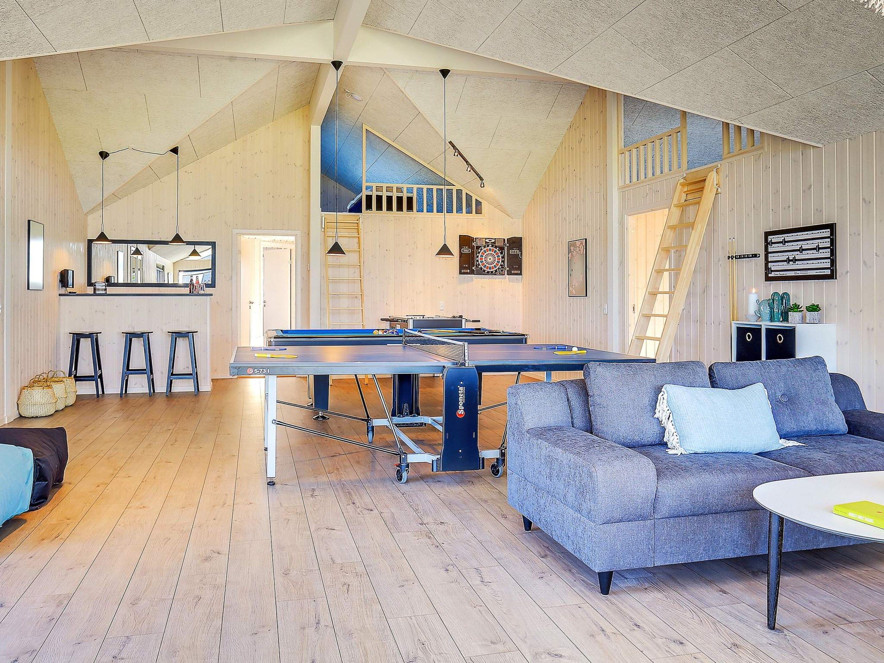 A spacious living area with a ping pong table, a sofa, and a kitchen area with a bar.
