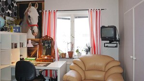 A room with a desk, a chair, a television, a horse painting, and striped curtains. - 6 Person Holiday Home in Vara (Vara)