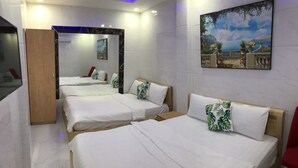 A hotel room with four beds arranged in a row, a wooden wardrobe, a large mirror, and a painting of a scenic landscape.