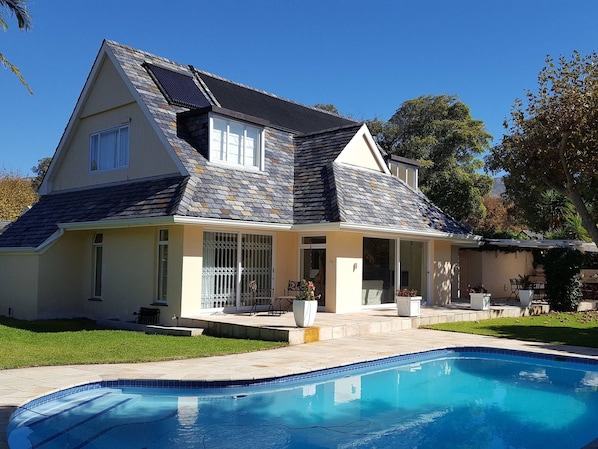 Une maison à deux étages avec une piscine, un patio couvert et un jardin aménagé.