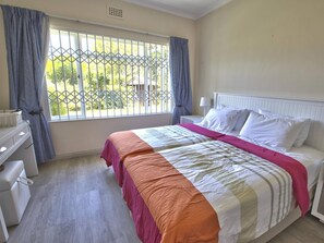 Une chambre à coucher avec un lit, une table de chevet, une commode et une fenêtre avec des rideaux.