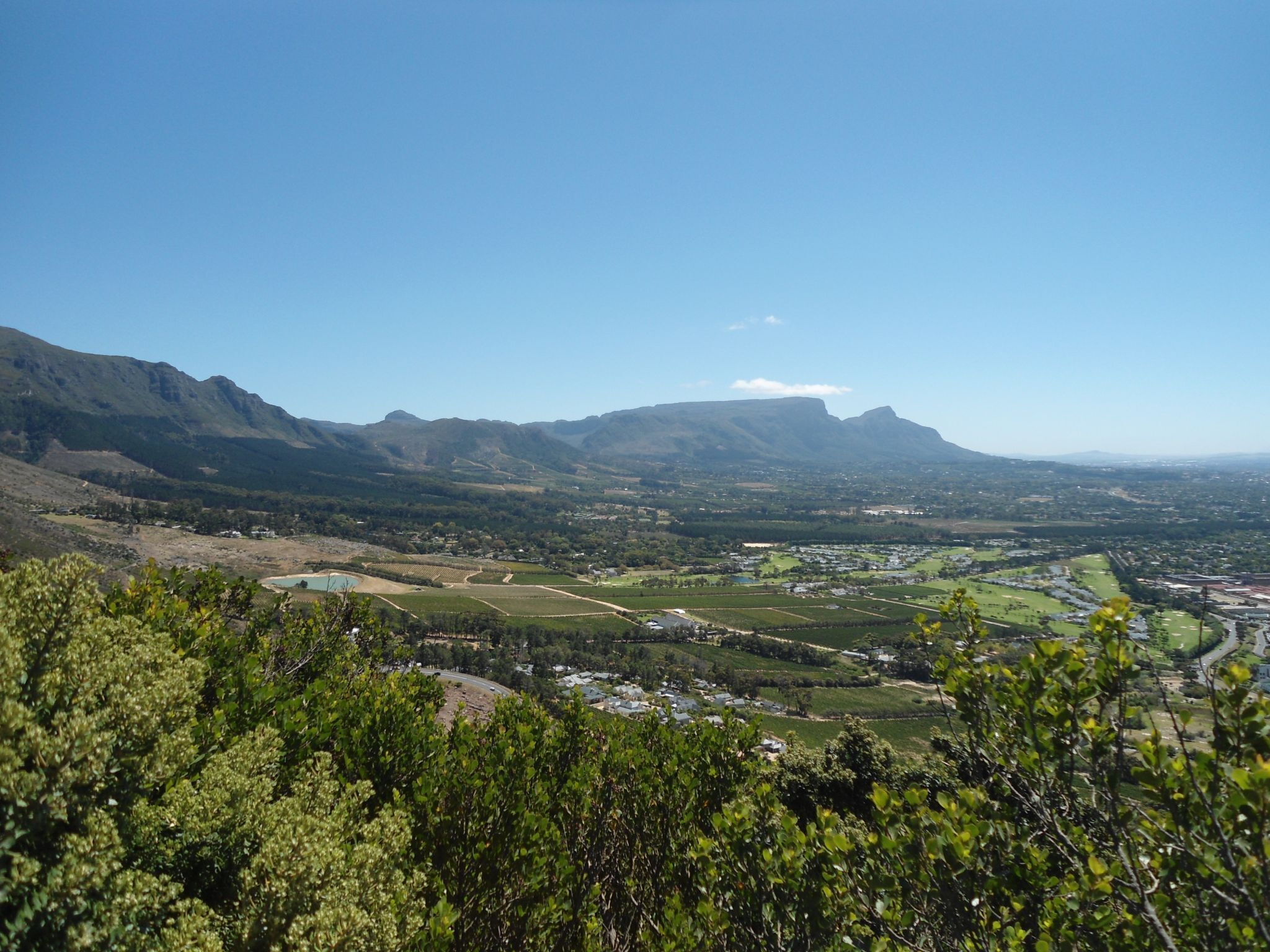 Una vista panorámica de un valle con montañas al fondo, un río y edificios dispersos.