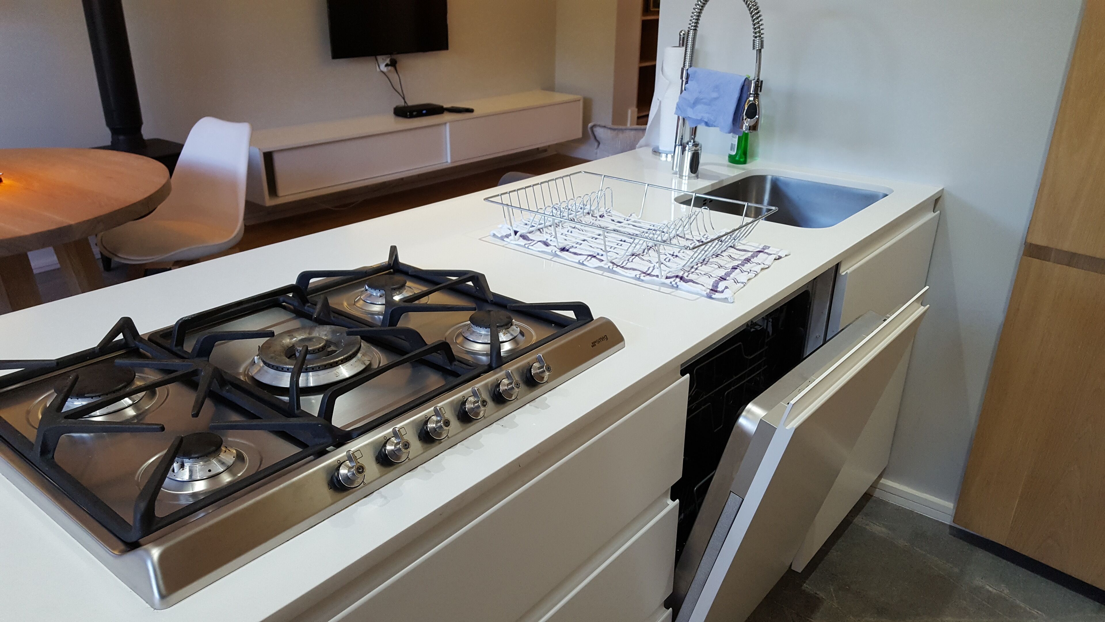 A kitchen with a stove, dishwasher, sink, and a small table with a chair.