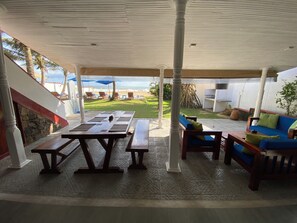 An outdoor patio with a table and benches, a blue sofa, and a view of the beach. - Tropical Beach House, Hikkaduwa (Hikkaduwa)