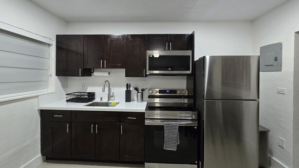A modern kitchen with dark cabinets, stainless steel appliances, and a white countertop. - Miami Health District • 2 Gbps Internet • 75” & 55” TVs • Stainless Steel (Miami)