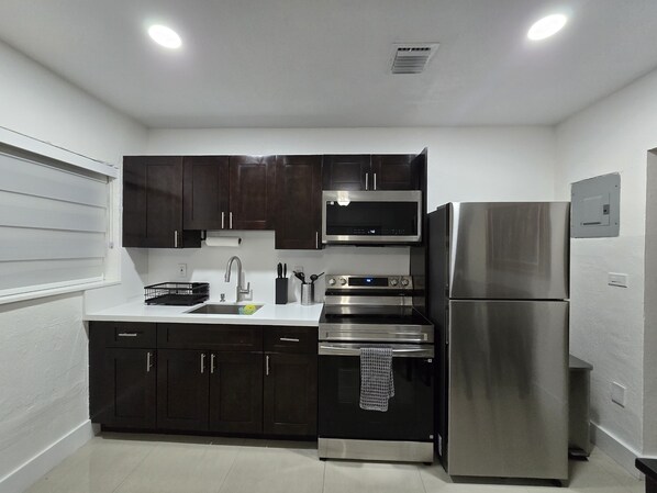 A modern kitchen with dark cabinets, stainless steel appliances, and a white countertop.