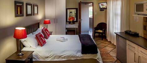 A hotel room with a bed, a desk, a chair, a television, and a kitchenette.