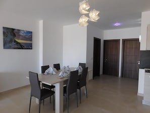 A dining area with a table set for four, chairs, a painting on the wall, and a modern light fixture.