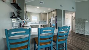 A modern kitchen with a central island, wooden chairs, and a built-in refrigerator. - Shore Thing - Corolla, Ocean Sands, 60 Yards to Beach, Ocean View, Pool, Hot Tub, Pets OK (Corolla)