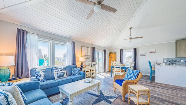 A spacious living area with a blue sofa set, a coffee table, wicker chairs, and a starfish-patterned rug. - Shore Thing - Corolla, Ocean Sands, 60 Yards to Beach, Ocean View, Pool, Hot Tub, Pets OK (Corolla)