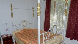 Una cama con dosel adornada con una colcha estampada, una mesita de noche con lámpara, y una ventana con cortinas.