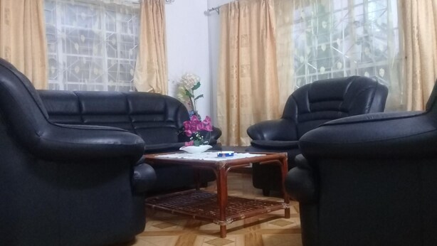 Una habitación con dos sofás de cuero negro enfrentados, una pequeña mesa de centro de madera con un jarrón de flores, y una alfombra estampada en el suelo.