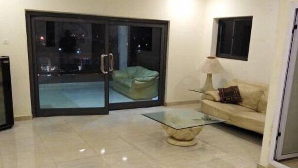 Ein Wohnzimmer mit Glastür zum Balkon, einer Couch, einem Glastisch und einer Lampe.