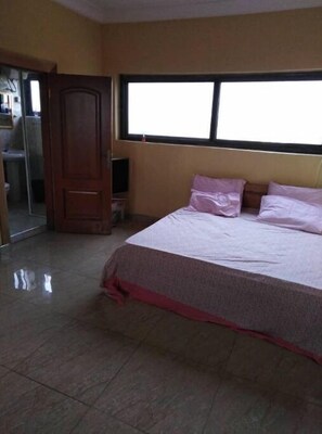 Relax in a spacious room with a large bed against a window, a tiled floor, and a wardrobe.