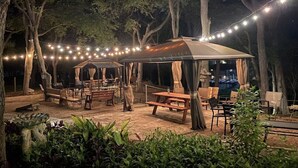 An outdoor patio area with string lights, wooden benches, and a covered seating area. - Bass Haus, Rustic Wundercove Cottage, Access to Shared Pool and River (New Braunfels)