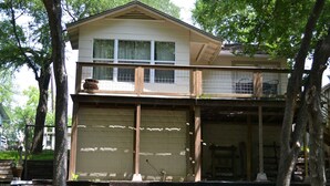 A two-story house with a garage, a balcony, and a wooden deck. - Bass Haus, Rustic Wundercove Cottage, Access to Shared Pool and River (New Braunfels)