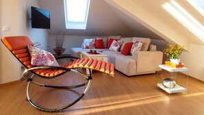 Un appartement moderne de style « loft » avec un plafond en pente, un fauteuil à bascule, un ensemble de canapés et un téléviseur à écran plat fixé au mur.