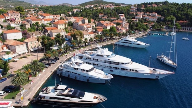 Un port de plaisance où sont amarrés plusieurs yachts, entouré d’une ville côtière aux bâtiments d’architecture traditionnelle.