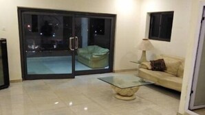 A living room with a glass door leading to a balcony, a sofa, a glass coffee table, and a lamp.