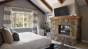 A bedroom with a stone fireplace, a bed with pillows, a desk, and a TV mounted above the fireplace. - Outpost: Granite Ridge Lodge 1: Private Hot Tub (Jackson)