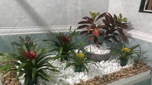 Een rechthoekige plantenbak met witte kiezelstenen en verschillende planten, waaronder een gele bloem, in een betegelde kamer.