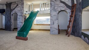 Um espaço de brincadeiras com um escorrega verde, parede de escalada e janela com vista.