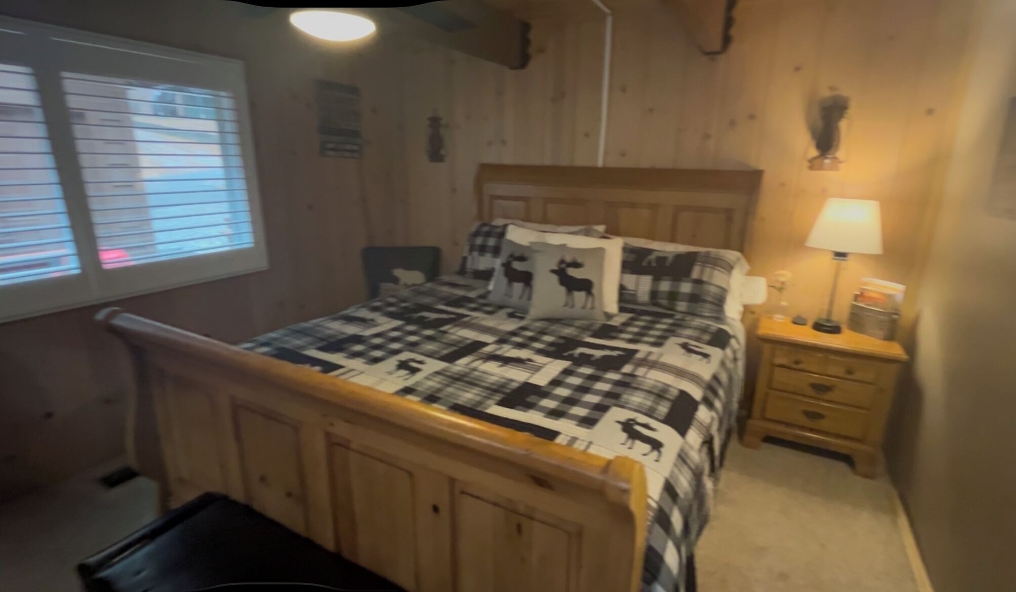 Un dormitorio de madera con una cama, una mesita de noche, una lámpara y una ventana con persianas.