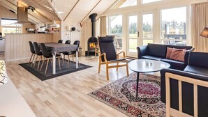 A spacious living area with a high ceiling, a fireplace, a dining table with chairs, a sofa, and large windows offering a view of the outdoors. - 6 Person Holiday Home in Hadsund-by Traum (Hadsund)