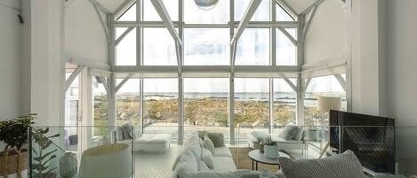 Un salon moderne avec une cloison en verre, des meubles blancs et un grand téléviseur.