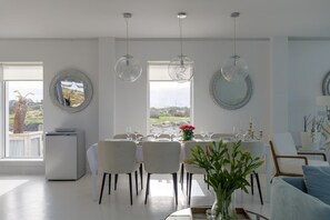 A dining area with a table set for six, surrounded by chairs, with a view of the outdoors through large windows.