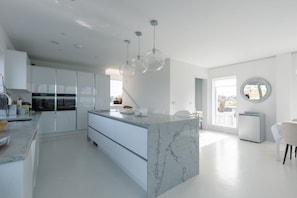 Une cuisine moderne dotée d’un îlot en marbre, de luminaires suspendus et offrant une vue sur l’extérieur.
