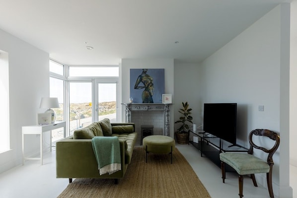 A modern living room with a sofa, a television, a fireplace, and a large window.