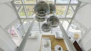 Una habitación con techos altos, ventanas amplias, un sofá blanco, una mesita redonda y lámparas colgantes esféricas.