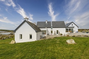 A white two-story house with a grey roof, a front porch, and a view of the sea.