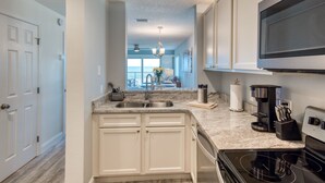 A modern kitchen with white cabinets, a black stove, and a large TV above the counter. - Tier 1. Oceanfront 2 bedroom, 2.5 bath townhouse. (St. Augustine)