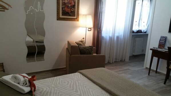 A hotel room with a bed, a chair, a lamp, a painting, and a window with curtains.