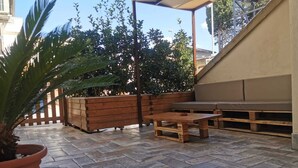 An outdoor patio area with a wooden bench, a table, and a potted plant.