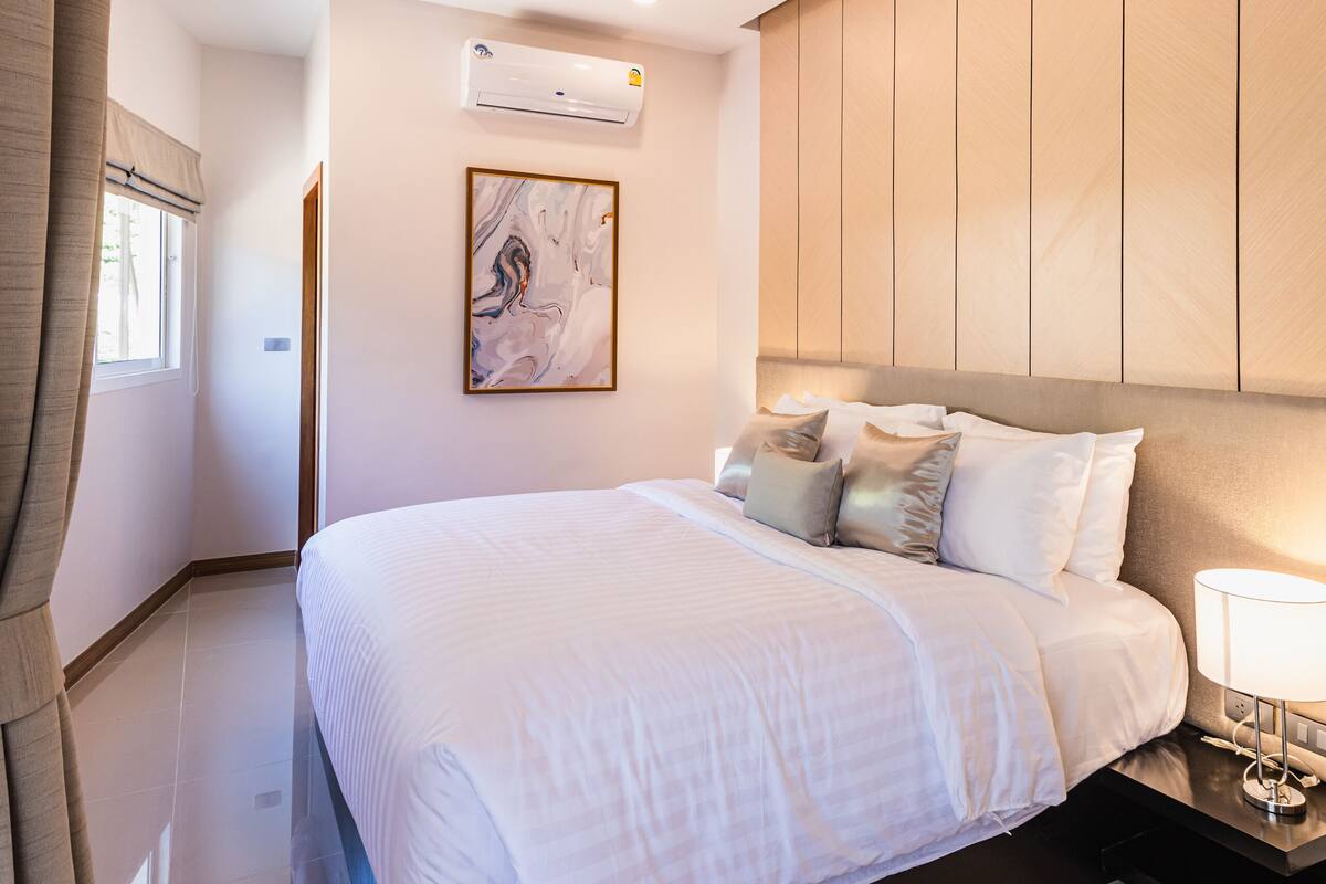 Una habitación de hotel moderna con una cama grande, una mesita de noche con lámpara, luz de techo y aire acondicionado instalado en la pared.