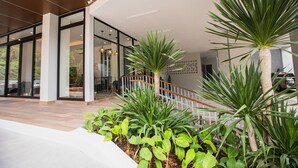 A modern building with a glass entrance, a wooden staircase, and various green plants. - Palmetto Condominium (Karon)