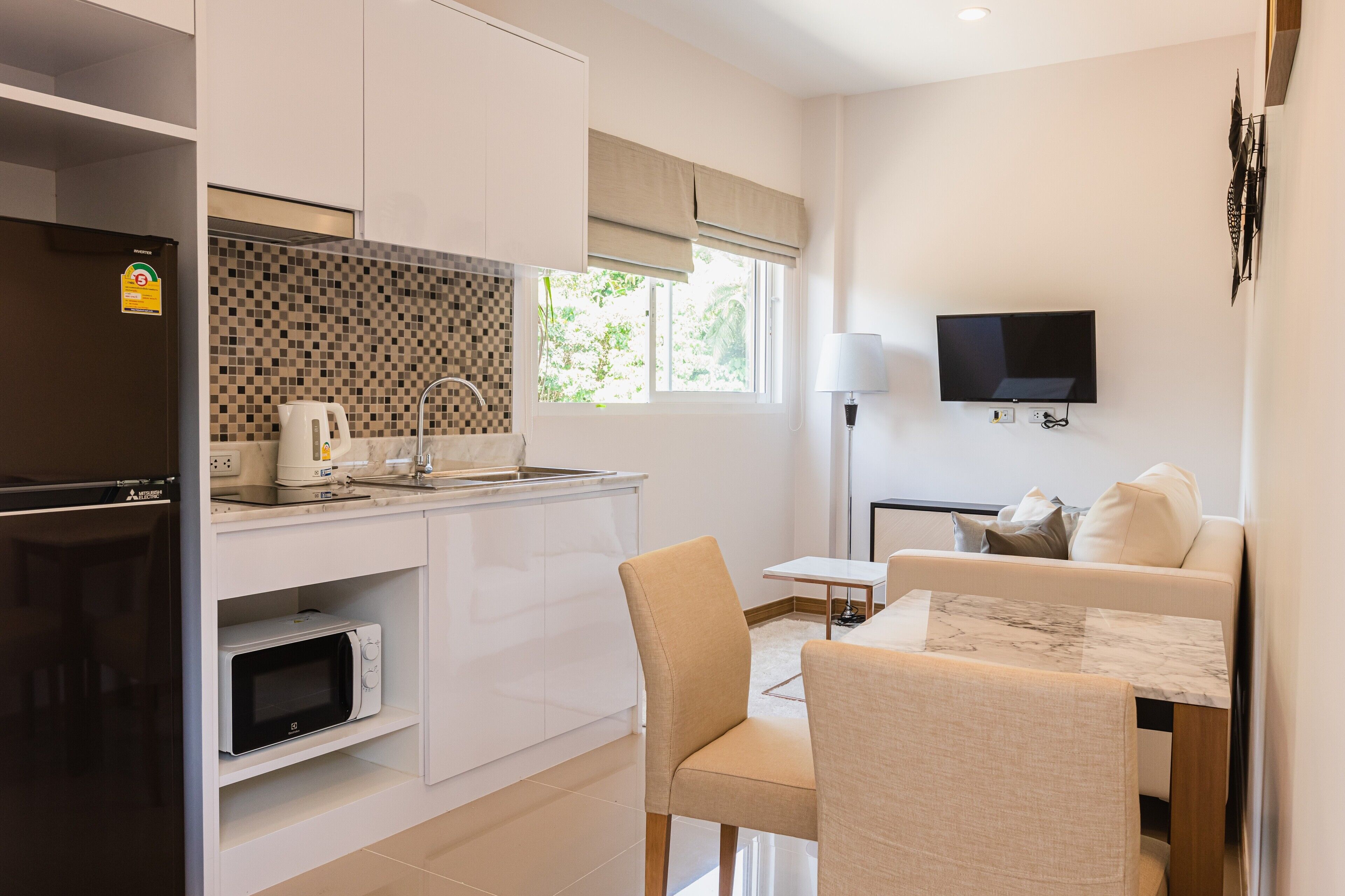 A modern kitchen with a microwave, sink, and refrigerator. There is a dining area with a table and chairs, and a TV mounted on the wall.