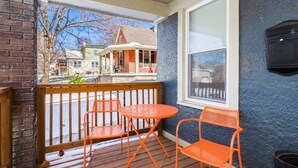 En veranda med to orange farvede stole og et bord, et vindue med udsigt til et hus, og en blå væg med struktur.